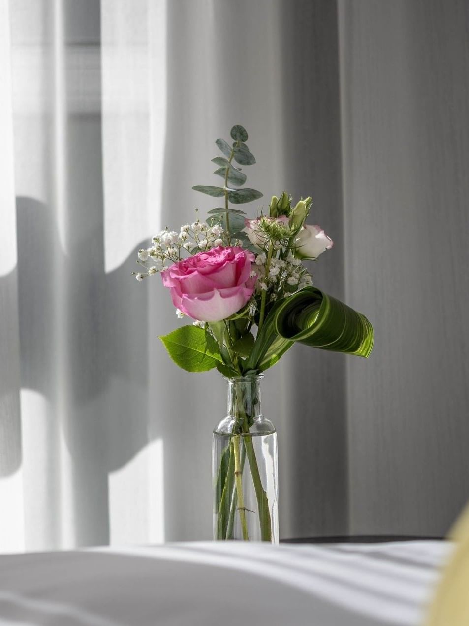 Vase with pink rose and green leaves on table next to bed at Warwick Le Crystal Montreal