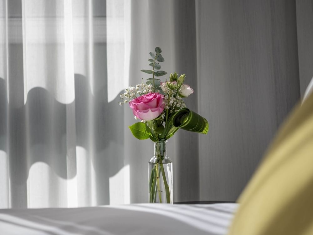 Vase with pink rose and green leaves on table next to bed at Warwick Le Crystal Montreal