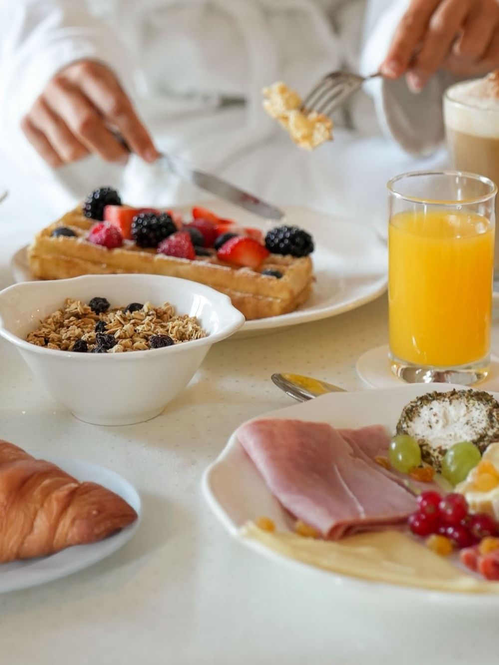 Gourmet breakfast spread with waffles, fruit, and coffee placed by a guest in a robe at Warwick Grand Place Brussels