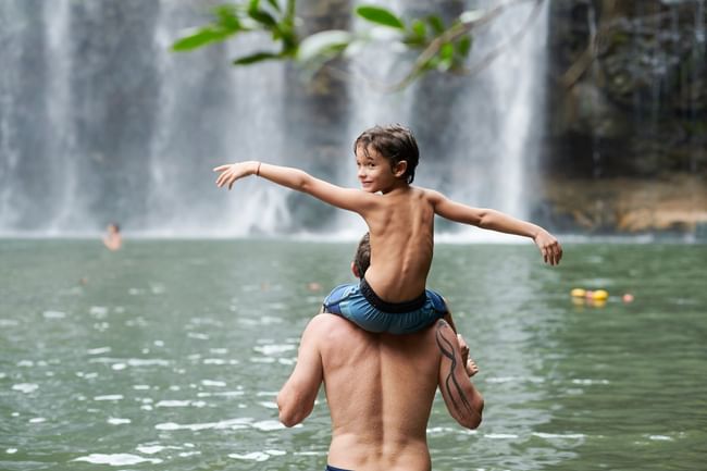 Father carries his son while enjoying a stunning tropical waterfall near Cala Luna Boutique Hotel