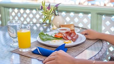 Plate with two fried eggs, bacon, sausage, and toast with juice and water on a table at Worthing Court Apartment