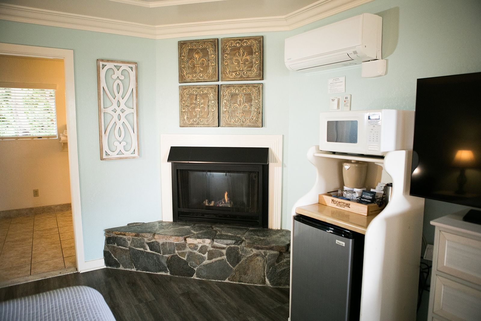 A hotel room with a stone fireplace, microwave, mini-fridge, and TV.