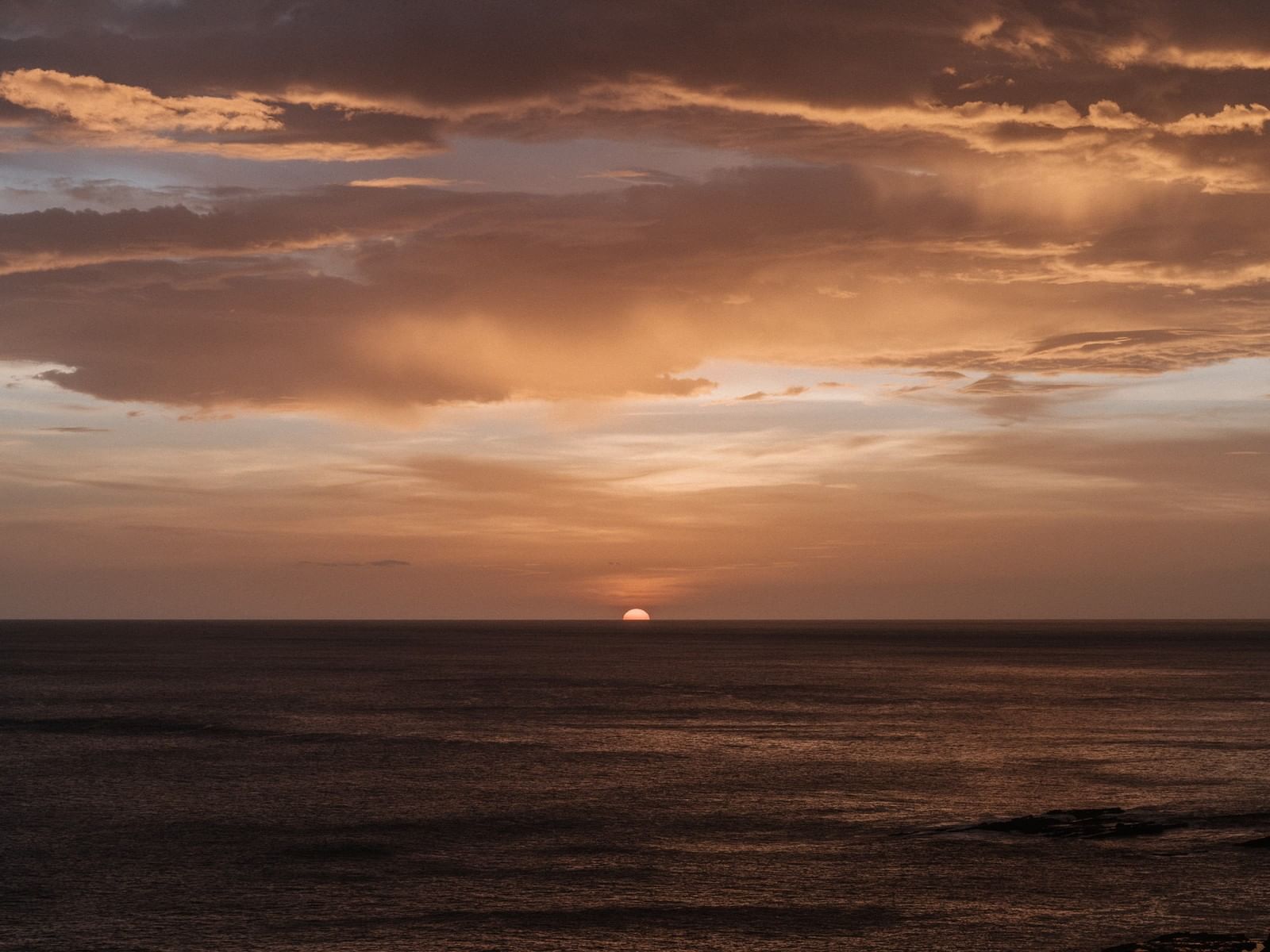 Sun setting on the horizon by a calm ocean under a warm orange-tinted sky near Morgan's Rock Reserve & Ecolodge