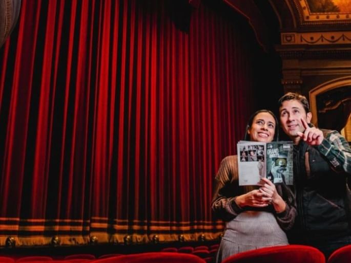 Couple holding a playbill booklet inside a grand theater auditorium room near Spencer Hotel & Conference Centre