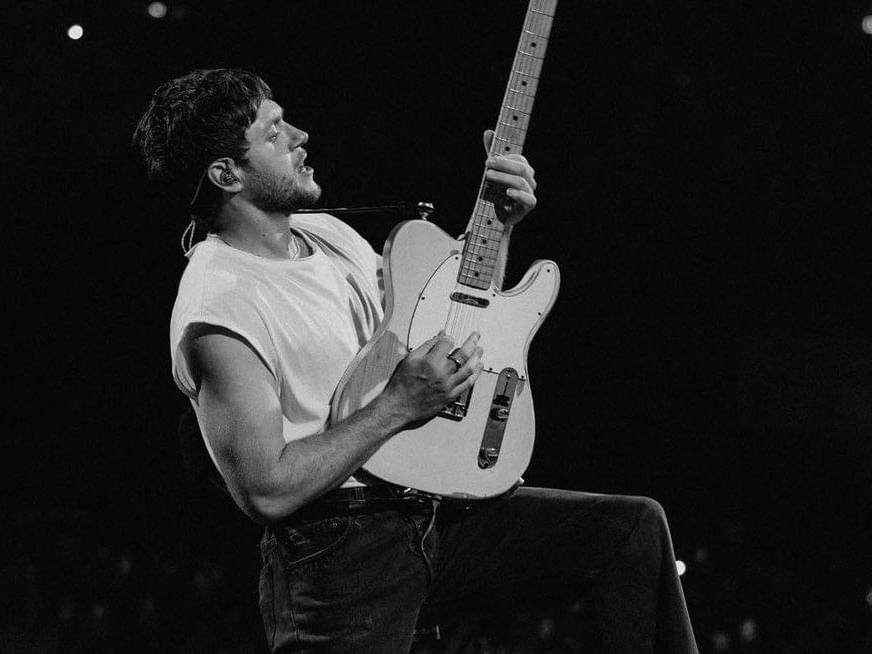 Black and white photo of a male musician playing an electric guitar on stage during a live performance