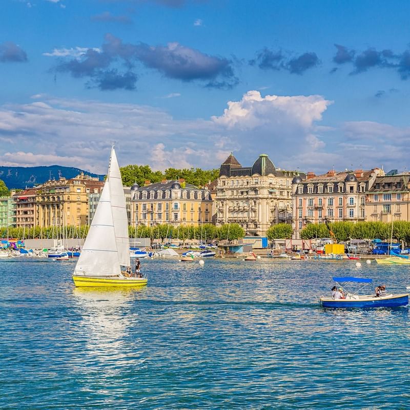 Sailboats glide through Geneva Lake near Warwick Hotels and Resorts with historical buildings and green trees under