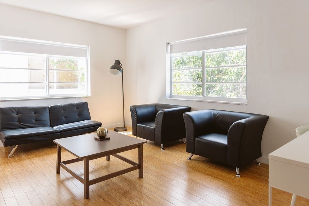 A wide view of a furnished living room with a couch, two chairs, a coffee table, and a floor lamp.