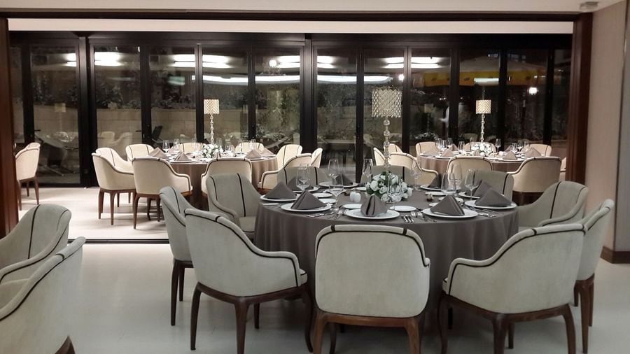 Plush chairs surrounding round tables with tall crystal lamps in a banquet hall at Warwick Ankara