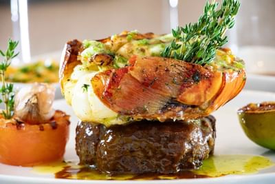 A lobster atop a steak with a sauce and herbs at Ellipse Grace Bay