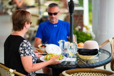 Couple dining on a patio by a glass-top table under an outdoor umbrella shade at Rodd Charlottetown Hotel