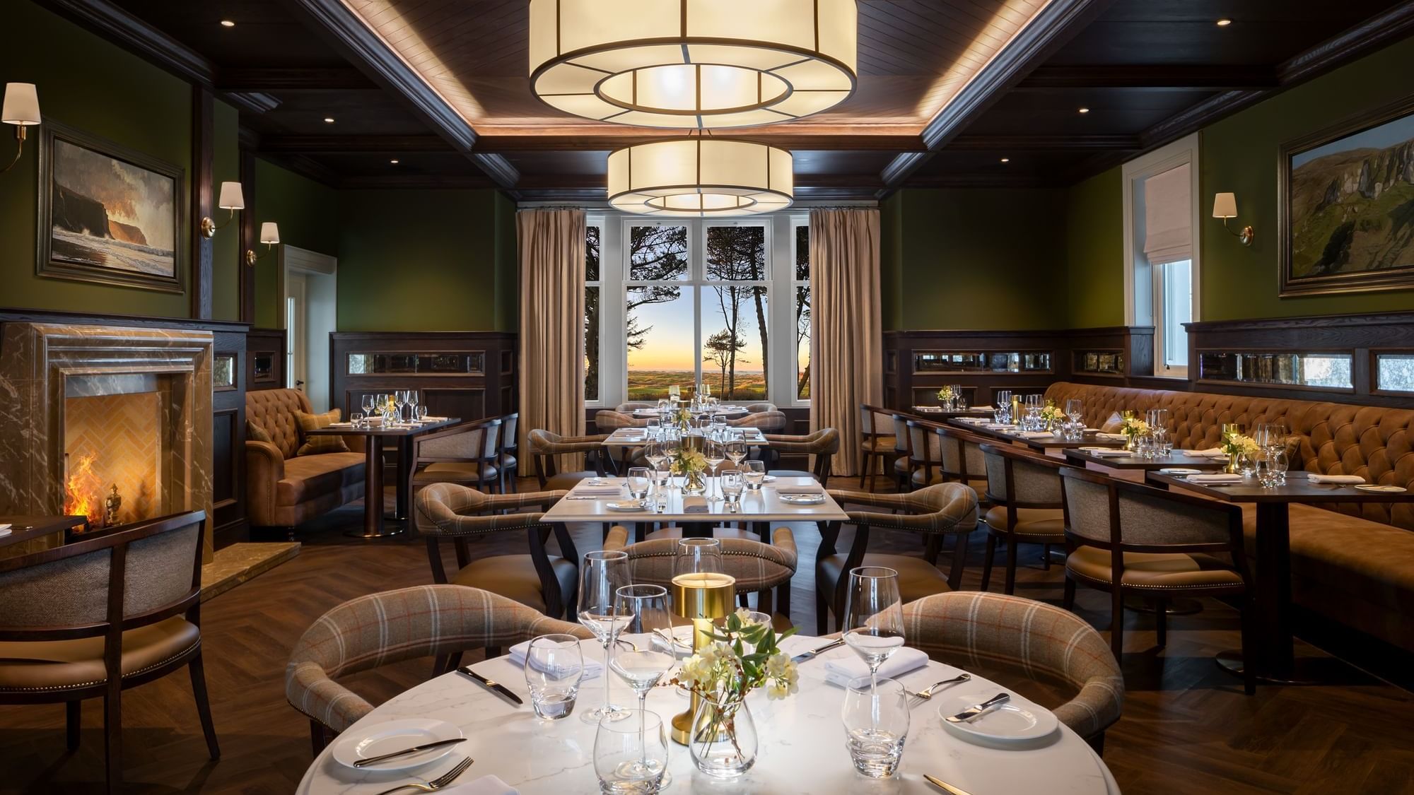 Dining area with fireplace glow, modern lights, sunset views, and tables set for dinner at Dunluce Lodge