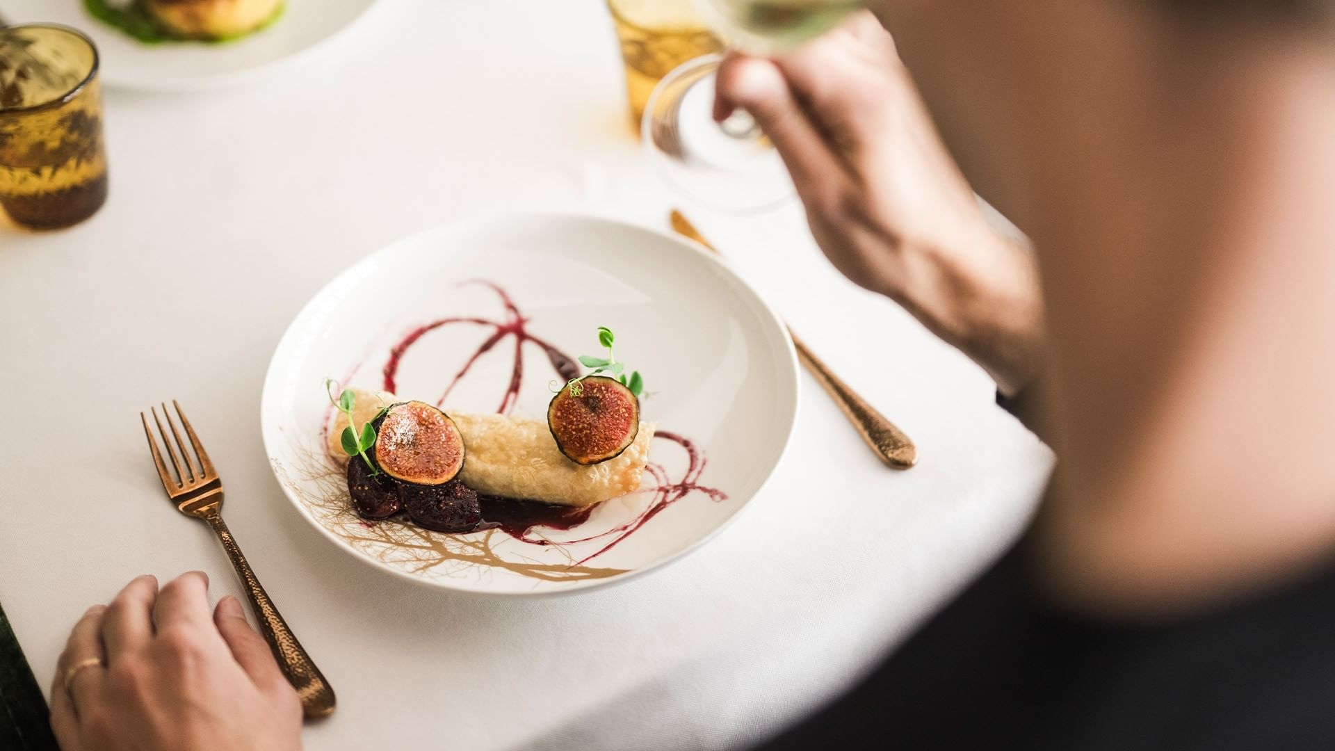 Person genießt ein Gericht mit Feigen auf einem Teller, während sie Wein trinkt.