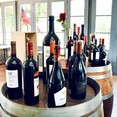 Wine Barrels Wine bottles in a wooden box by a red rose on oak barrels under a glass window at NOI Blend Colchagua