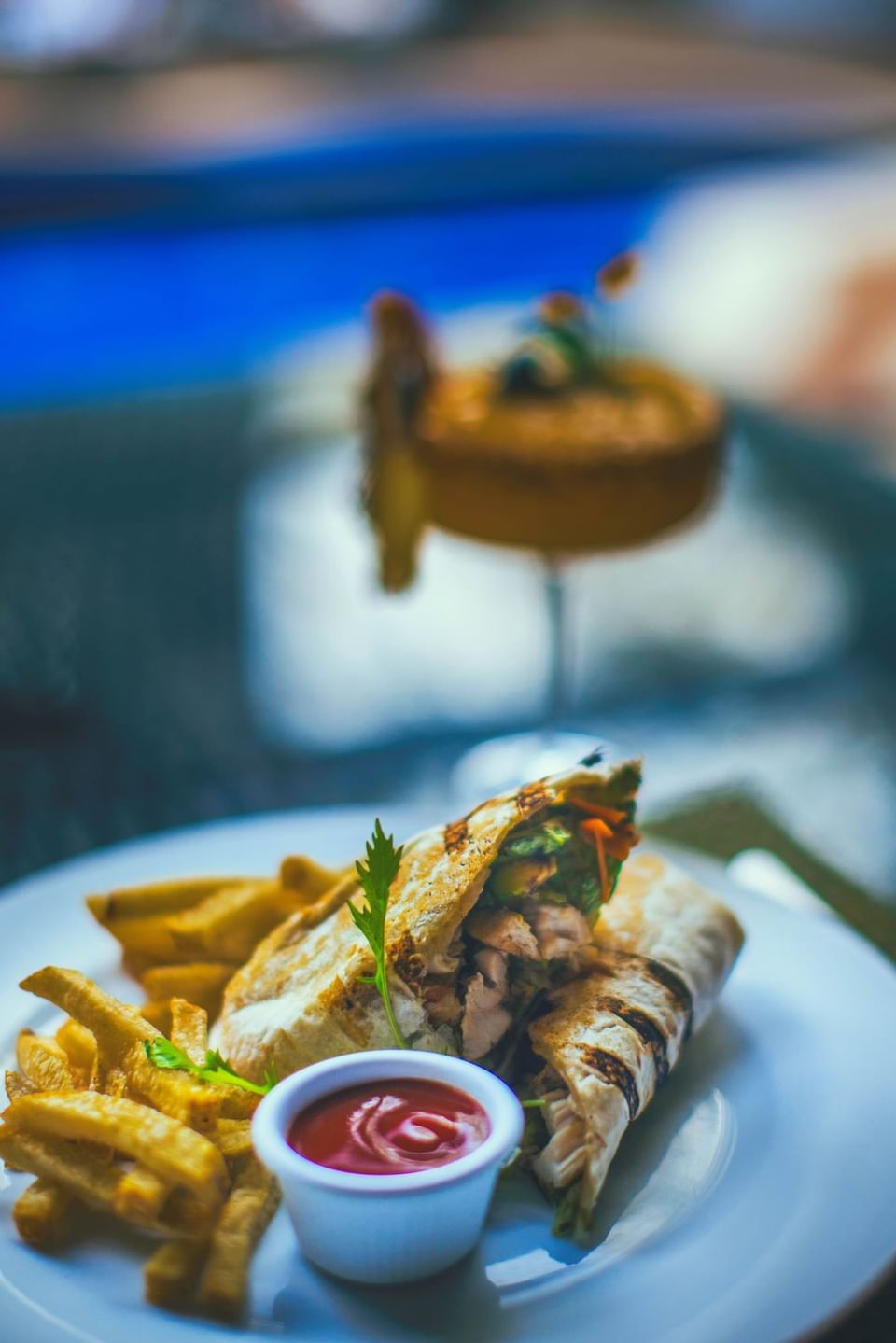 Grilled chicken wrap with french fries and ketchup next to a cocktail in Sloth Restaurant at Jungle Vista Boutique Hotel