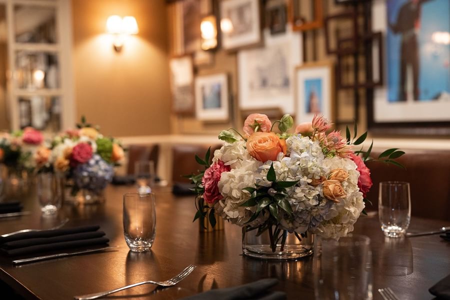 Floral centerpiece by wine glasses on a dark wood table under a warm lamp at Warwick Melrose Dallas