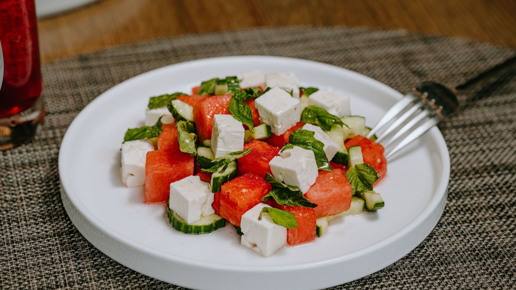 Plate of watermelon salad with feta and cucumber, garnished with mint leaves, served with a fork.