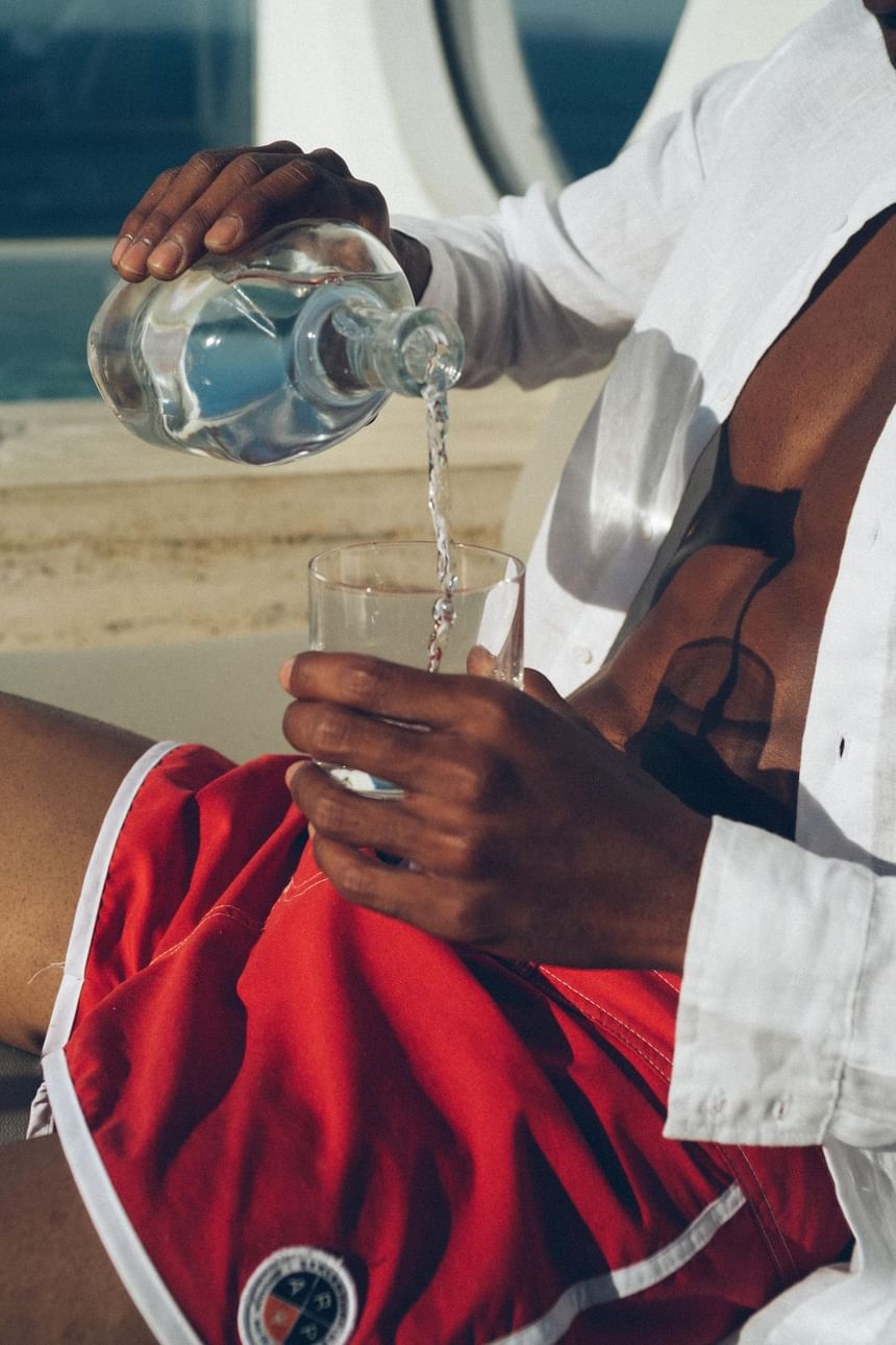 Homem com short vermelho e camisa branca se servido de uma água no Janeiro Hotel com bar na piscina