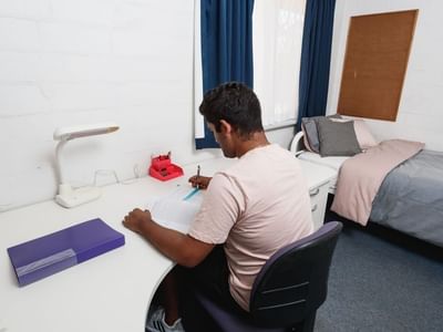 Man studying at desk with bed in room at UniLodge at Curtin University - Vickery House.