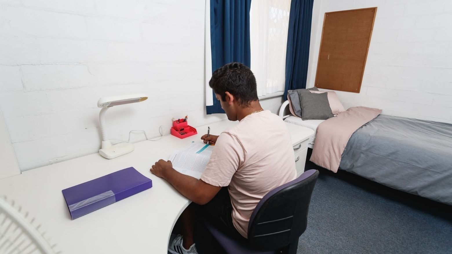 Man studying at desk with bed in room at UniLodge at Curtin University - Vickery House.