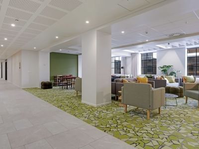 Modern communal lounge with colorful armchairs, patterned carpet, and large windows at UniLodge Auckland Central.