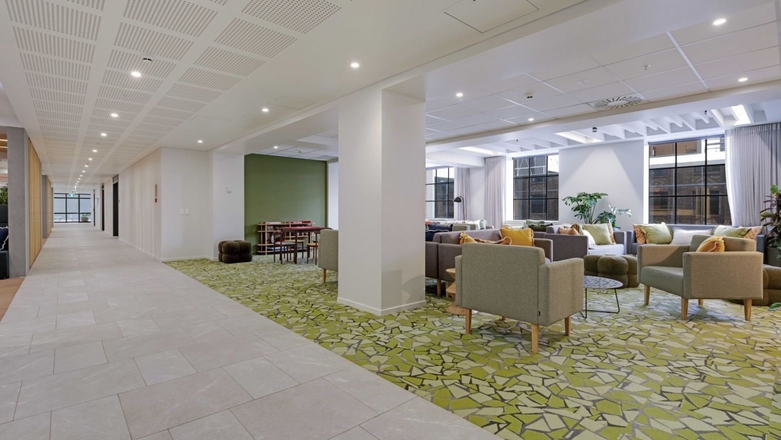 Modern communal lounge with colorful armchairs, patterned carpet, and large windows at UniLodge Auckland Central.