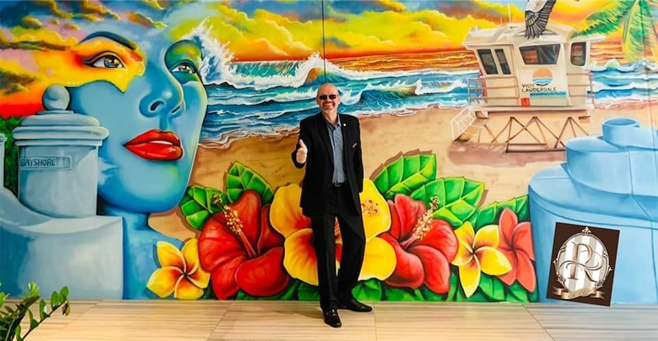 Man stands in front of a mural featuring ocean waves, a woman's face, and flowers near Riverside Hotel Fort Lauderdale