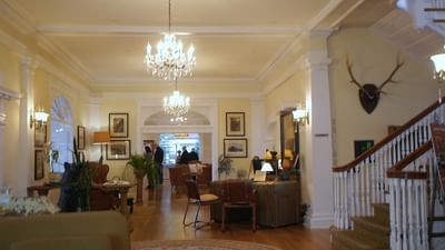 A warm, elegant hotel lobby with multiple chandeliers and a curved staircase at The Stanley Hotel