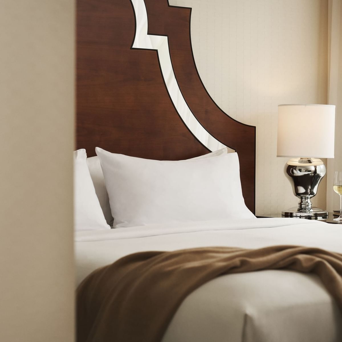 A bed with two pillows, a blanket, and a nightstand with a lamp and wine glass.