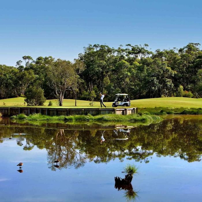 Golf course with a cart and players reflected in a tranquil pond near Mercure Kooindah Waters