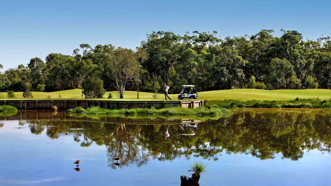 Golf course with a cart and players reflected in a tranquil pond near Mercure Kooindah Waters