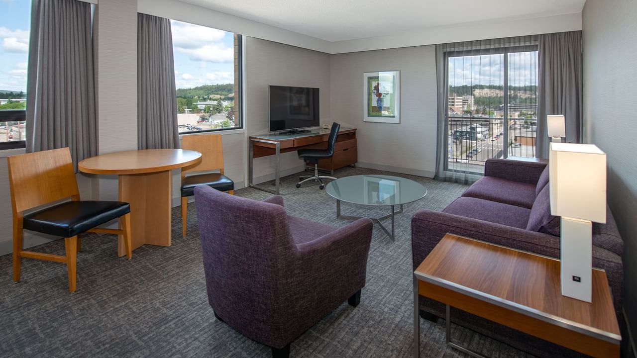 Suite with a couch, desk, chair, round table, and glass table with a city view.