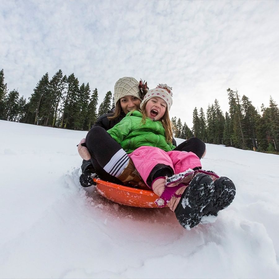 Mother and daughter sledding down our sledding hill in a plastic saucer sled