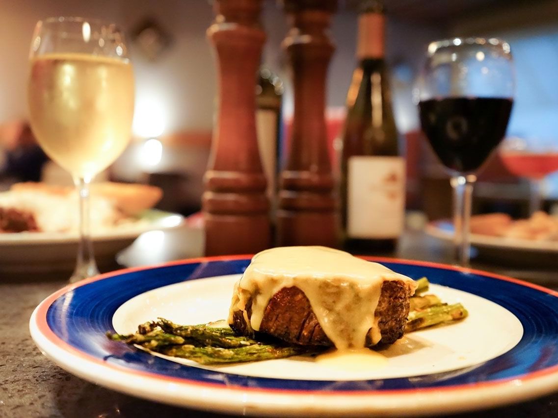 Filet mignon topped with cream sauce and asparagus, served with wine in Doe’s Eat Place near The Markham Hotel