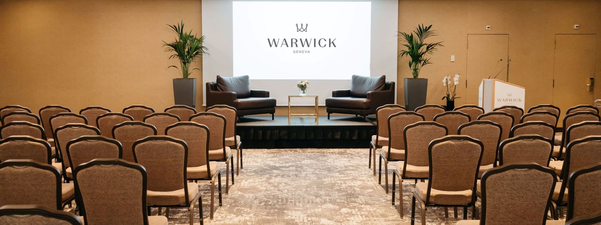 Leather armchairs by a gold table on a stage in front of guest chairs in Mont-Blanc + Jura at Warwick Geneva