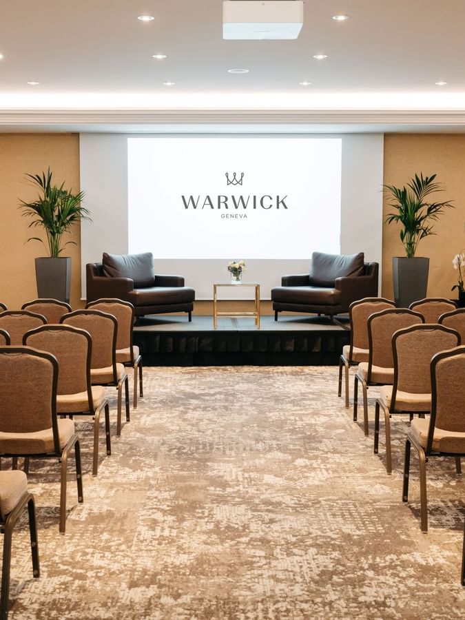 Leather armchairs by a gold table on a stage in front of guest chairs in Mont-Blanc + Jura at Warwick Geneva