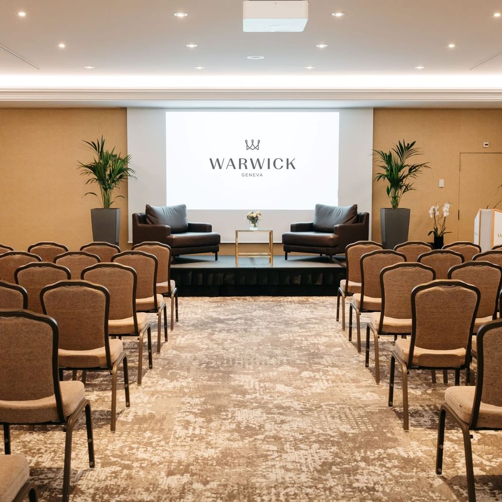 Leather armchairs by a gold table on a stage in front of guest chairs in Mont-Blanc + Jura at Warwick Geneva