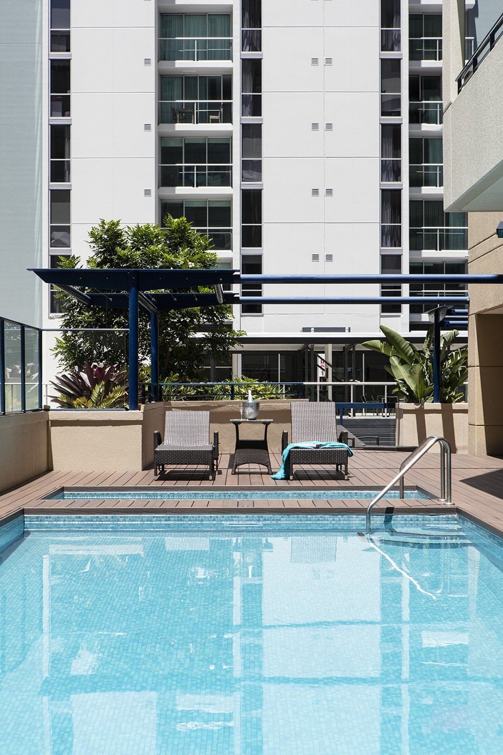 Outdoor swimming pool with two lounge chairs and an umbrella on the deck outside the building at The Sebel Brisbane