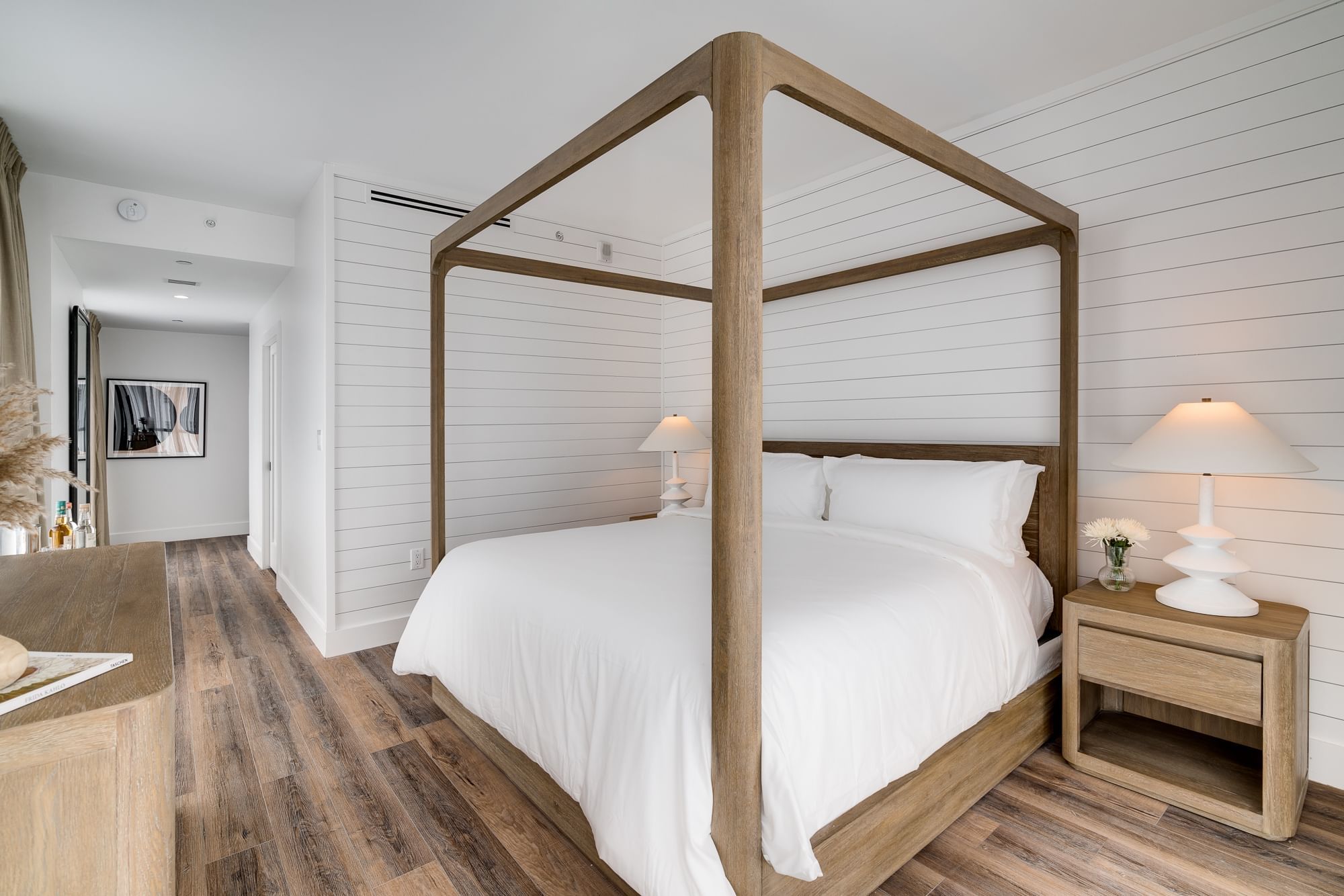 A clean and modern bedroom with a four-poster bed, wooden nightstand, and shiplap wall.