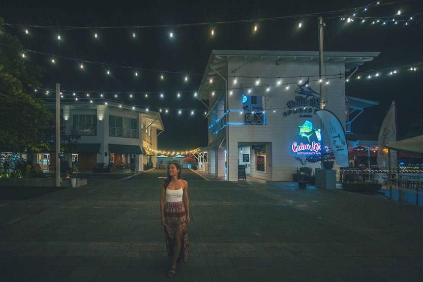 Woman walking under string lights in a night plaza with a restaurant at Marina Pez Vela near Jungle Vista Boutique Hotel