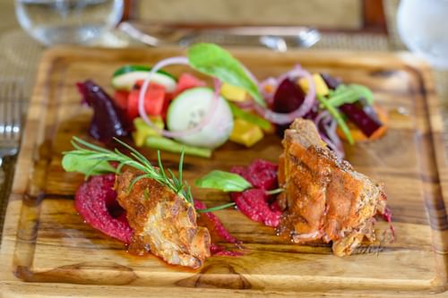 Roasted meat with beet puree and garden salad on a wooden board at La Bastide Restaurant, Morgan’s Rock Reserve & Ecolodge