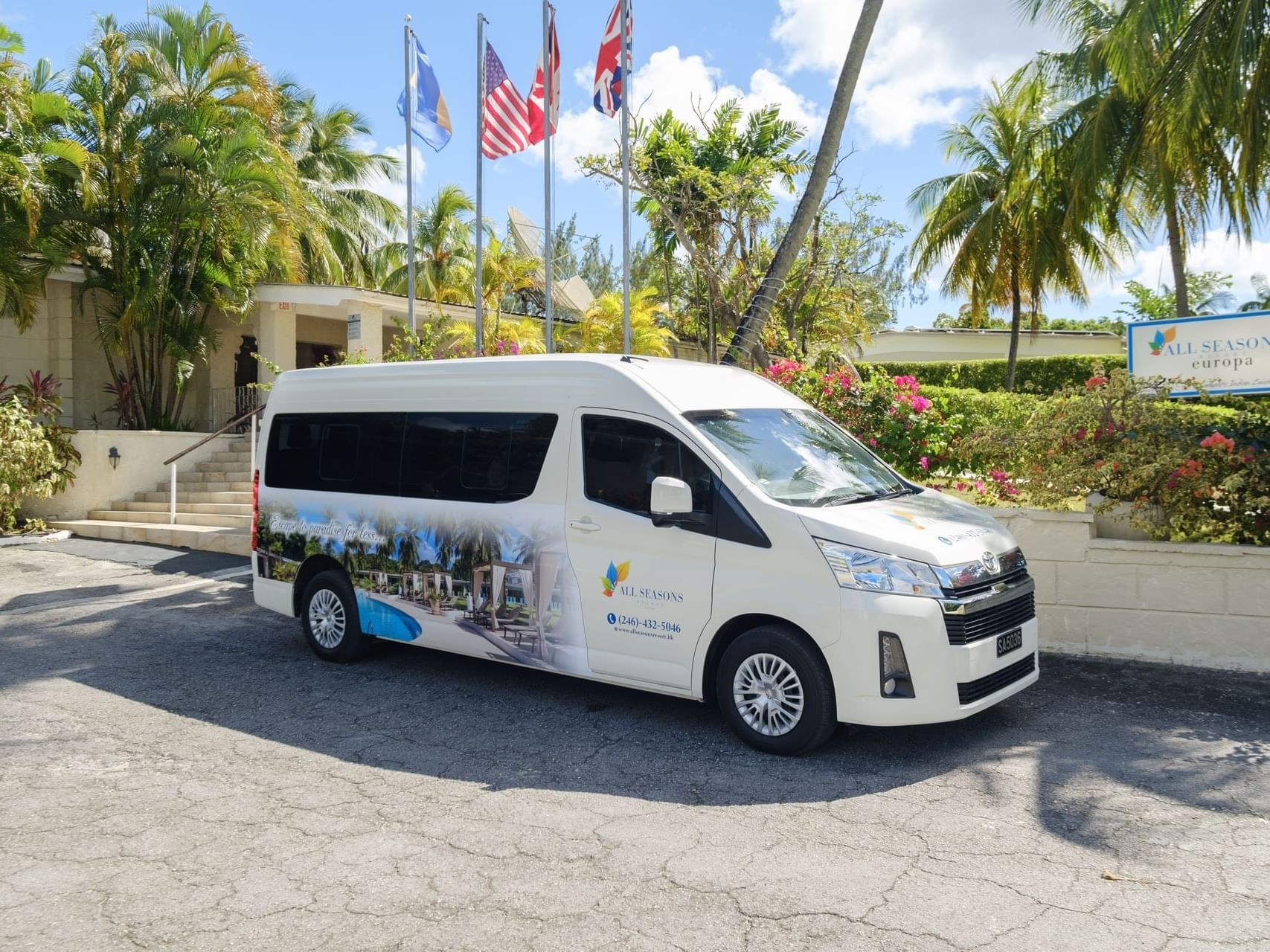 A white shuttle van with decals parked outside by trees and multiple flags at All Seasons Resort Europa