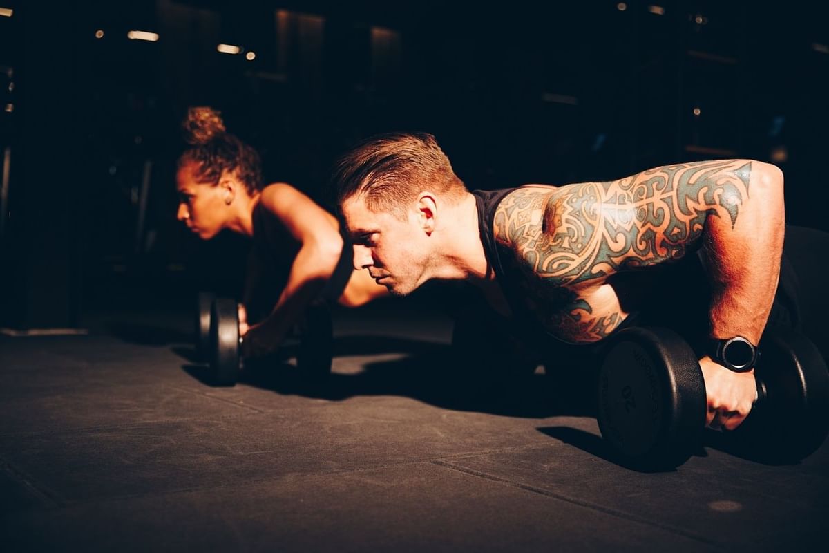 Woman and man doing pushups with dumbbells in gym at The May Fair Hotel