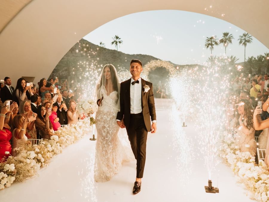 A stunning wedded couple walks down the aisle through beautiful sparkles at Marquis Los Cabos Resort.