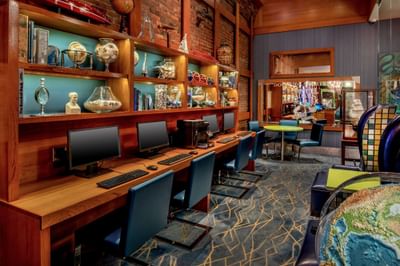 Computer workstations beneath lit wooden shelves against a brick wall in Lobby Business Center at Harborside Inn Boston