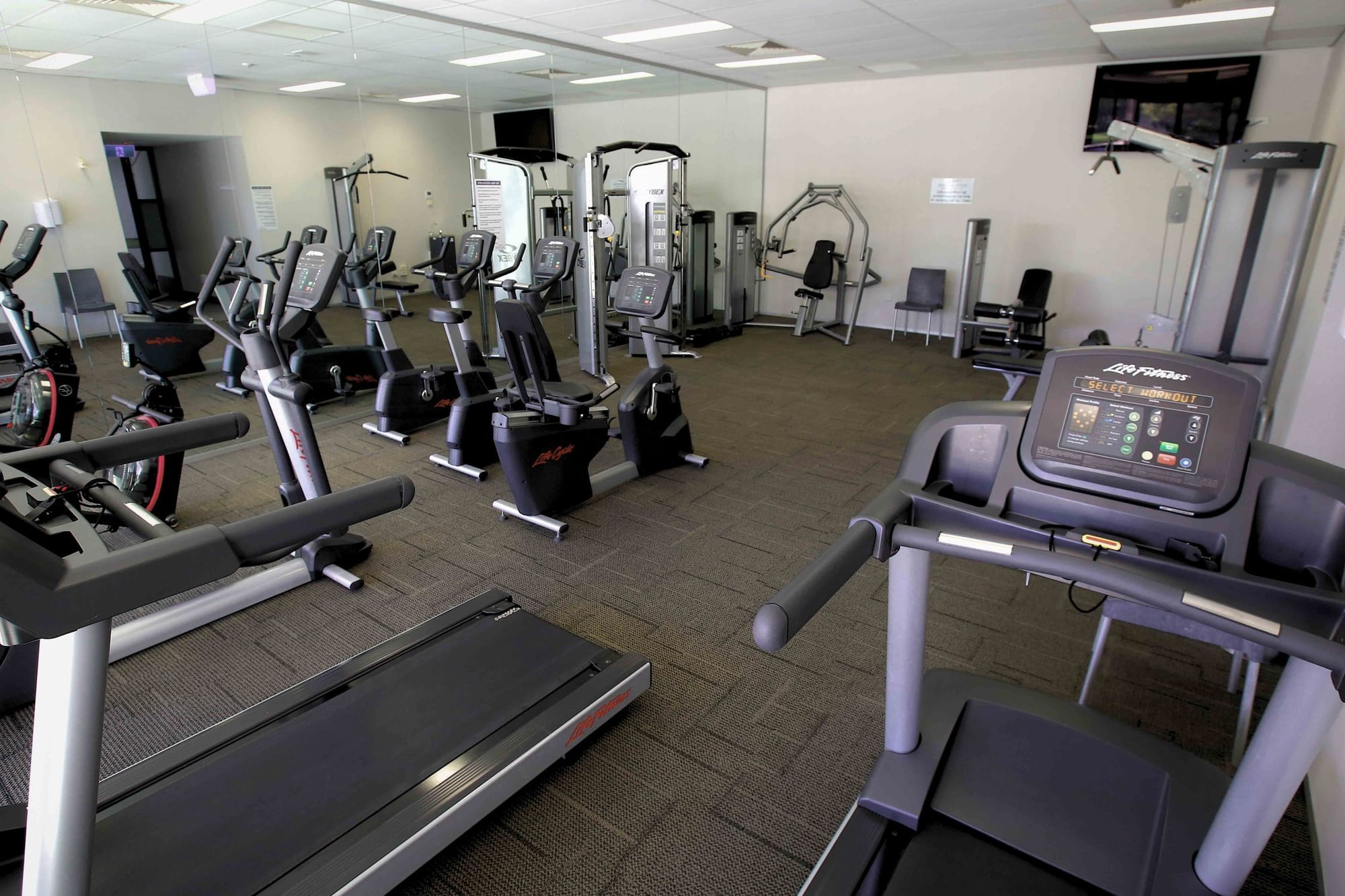 Gym with treadmills, elliptical machines, weight machines, and a mirrored wall reflecting the workout area.