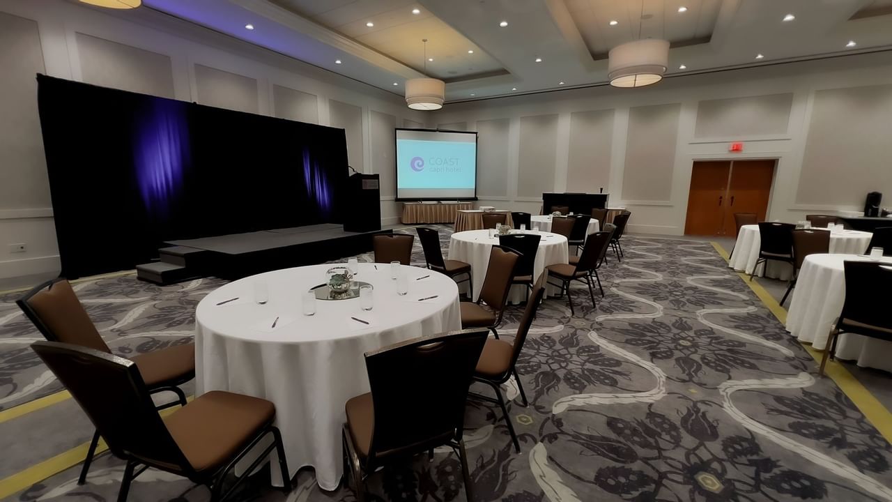 Ballroom with round tables, chairs, stage, podium and presentation screen