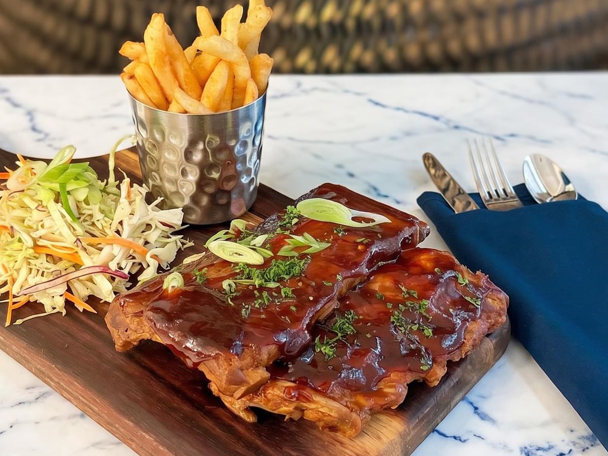 Ribs, fries, and coleslaw on a wooden board.