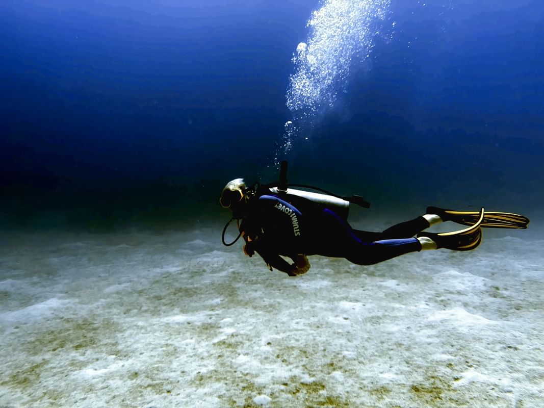 Scuba diver by the sandy floor under deep blue water surrounding rising bubbles near Warwick Paradise Island Bahamas