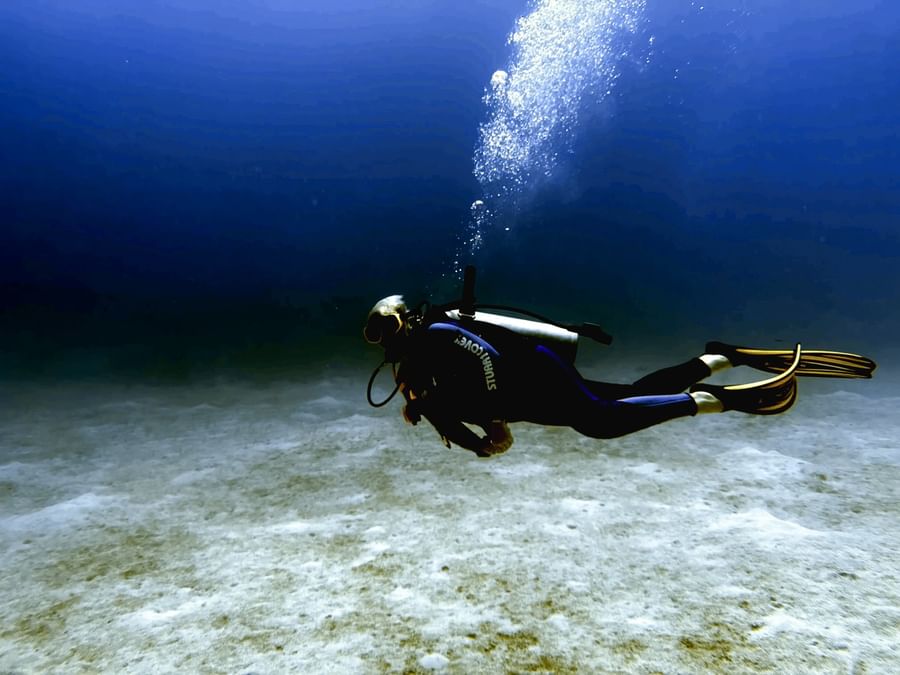 Scuba diver by the sandy floor under deep blue water surrounding rising bubbles near Warwick Paradise Island Bahamas