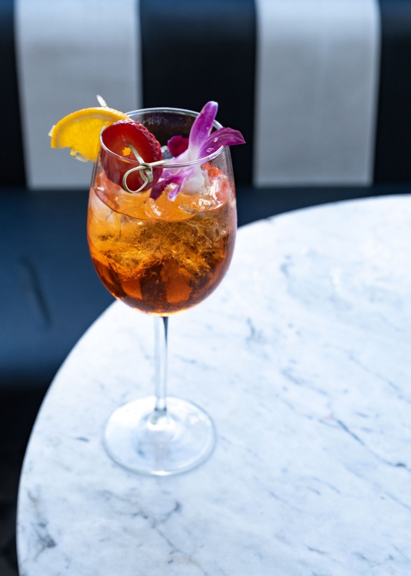 a cocktail with ice and garnishes in a stemmed glass on a marble table